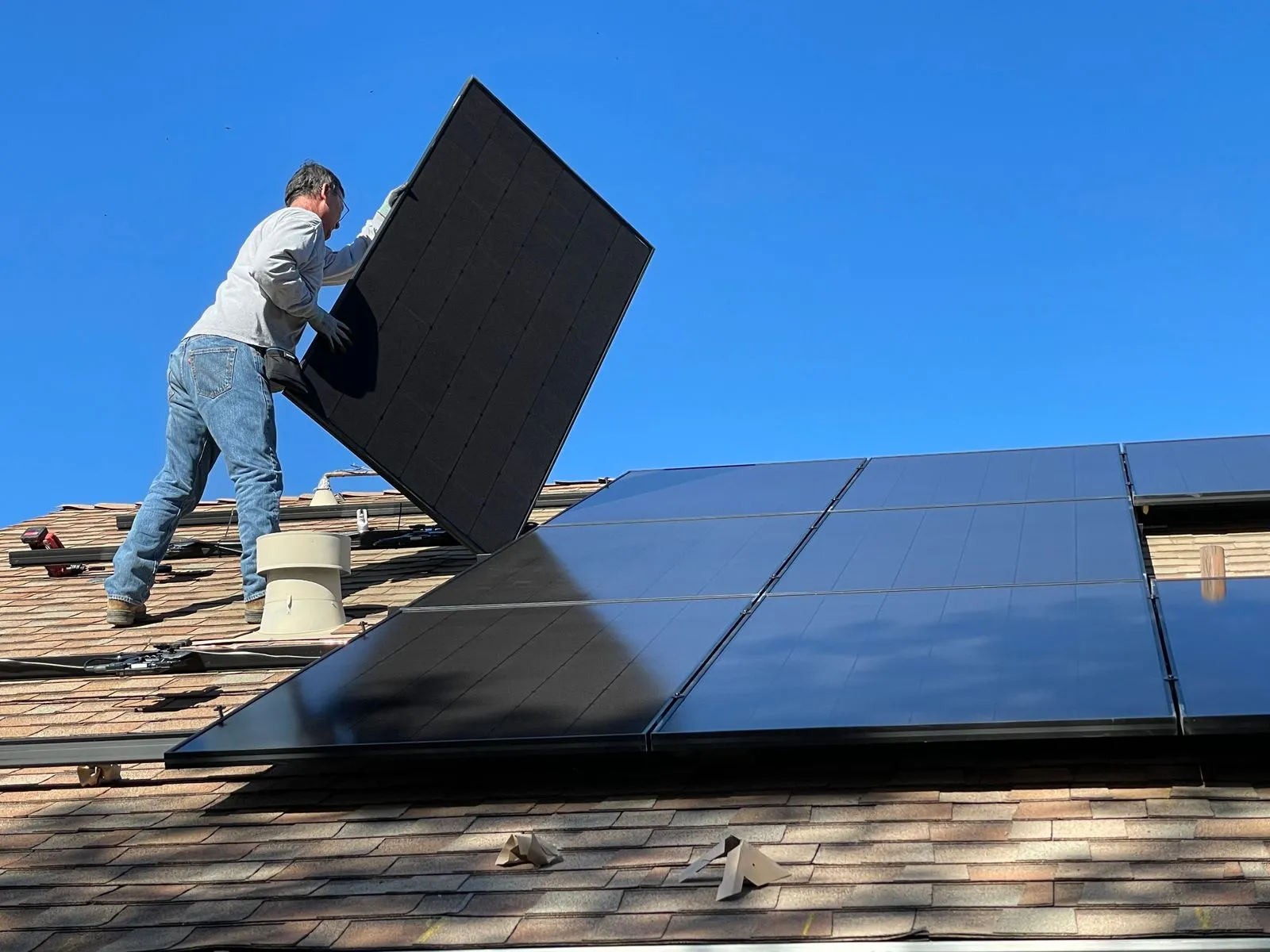 Monteur trägt ein PV-Modul auf einem Dach